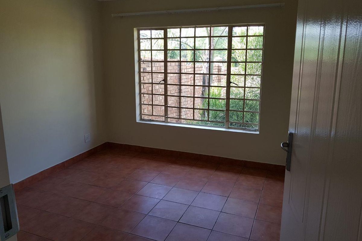 An empty bedroom featuring tiled flooring and a window with security bars, offering a blank canvas for personalization.