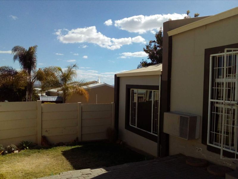 Rear exterior view of the townhouse featuring a small paved patio, lawn, precast boundary wall, and window-mounted air conditioning unit.
