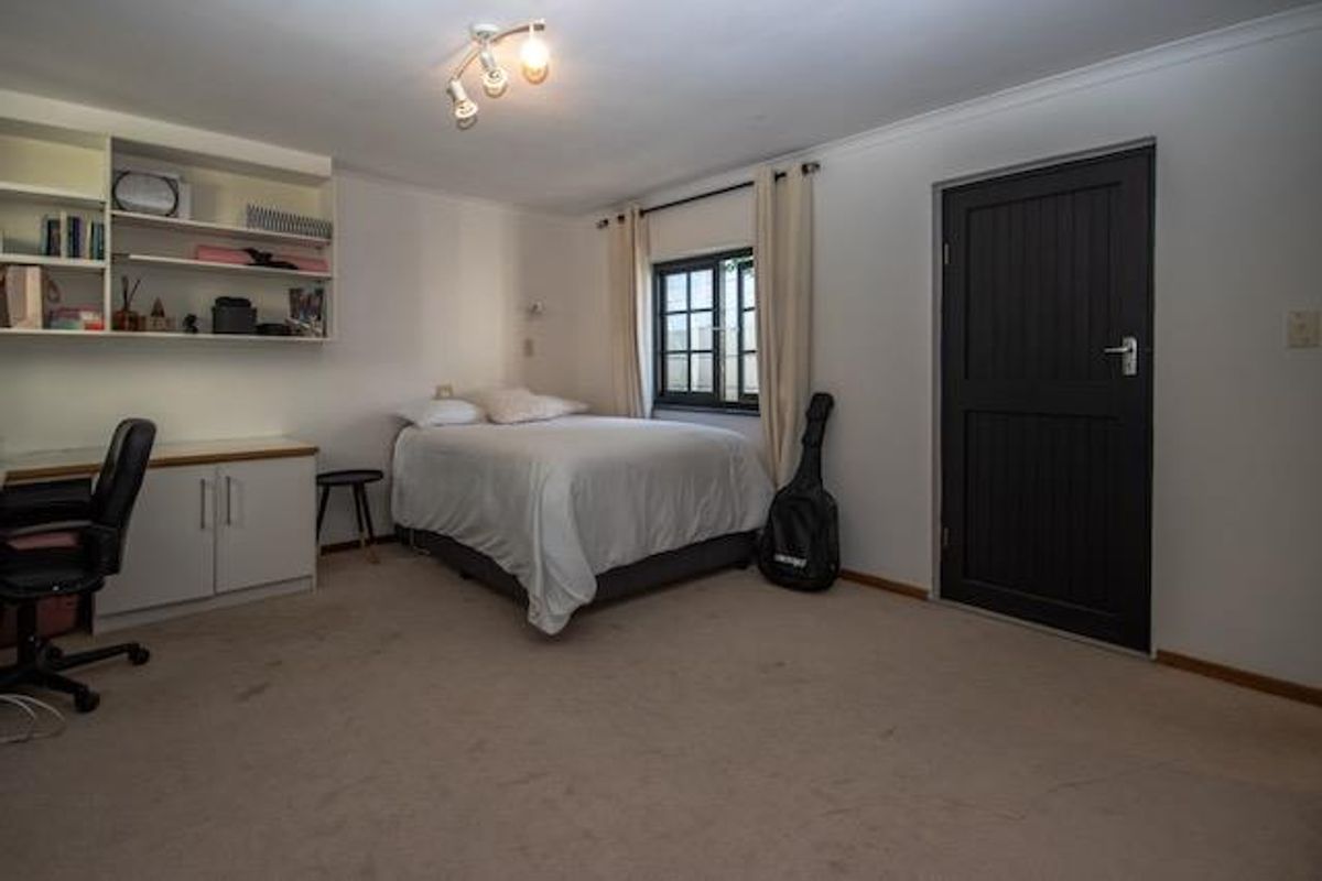 A functional bedroom featuring built-in shelving, a desk area, and neutral carpeting, offering a versatile space for rest or study.