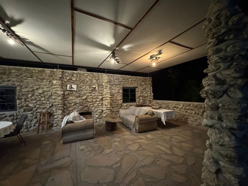 Spacious covered outdoor patio featuring rustic stone masonry walls, flagstone flooring, and exposed beam ceiling, ideal for evening entertainment.