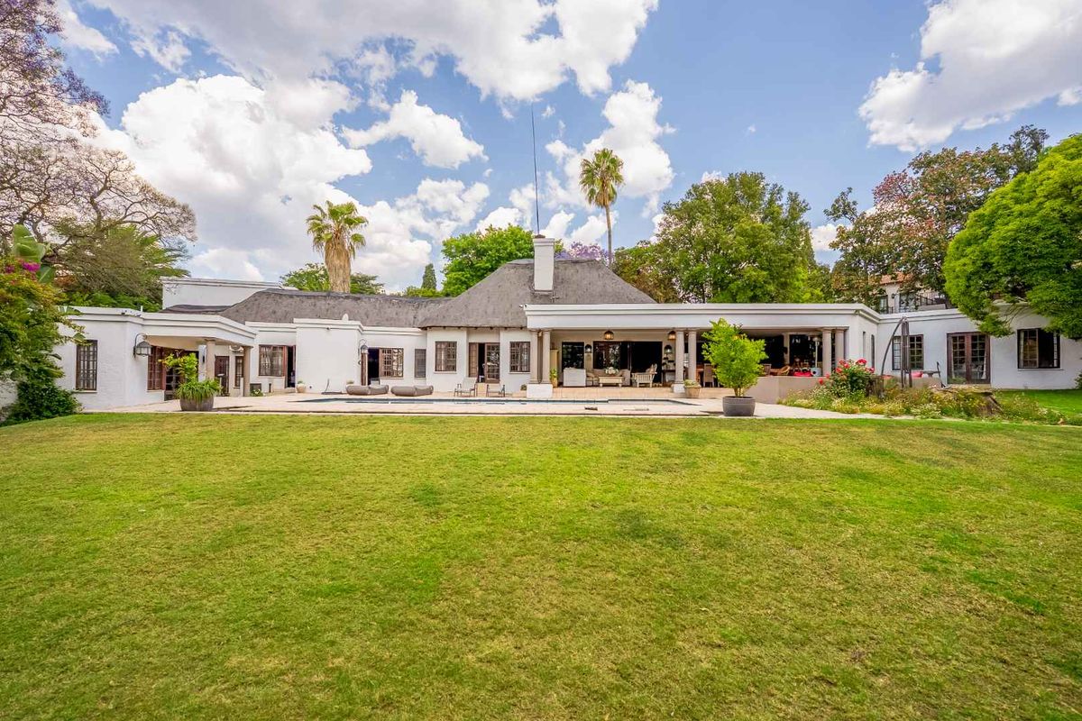Spacious rear exterior view featuring a large manicured lawn, a swimming pool, and a covered patio area attached to the main residence.