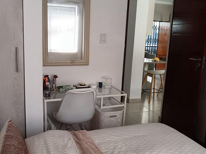 A bedroom featuring built-in wardrobe storage and tiled flooring, with a view through the doorway into an adjacent living area.