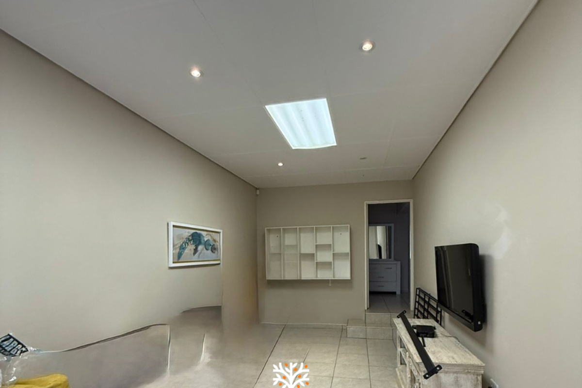 A neutral living room featuring tiled flooring, recessed ceiling lighting, and built-in wall shelving, providing a functional and versatile living space.