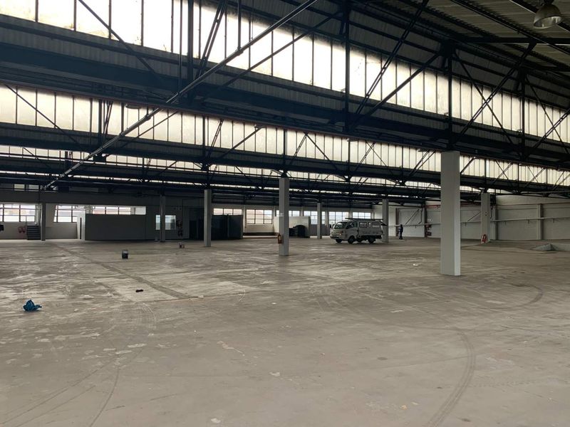 Expansive open-plan industrial warehouse space featuring high ceilings with exposed steel trusses, abundant natural light from clerestory windows, and durable concrete flooring.