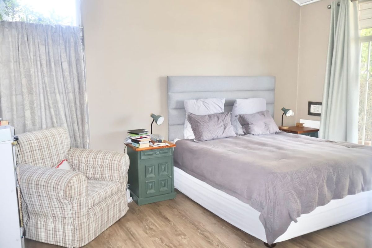 A well-lit bedroom featuring neutral wall tones, wood-look flooring, and large windows with curtains.
