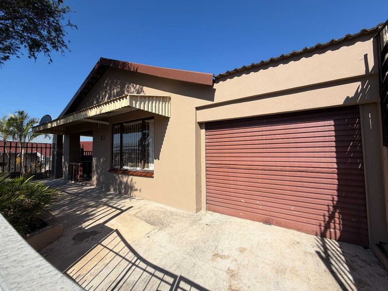 Front elevation of a single-story house featuring a roller garage door, concrete driveway, and security bars on the windows.