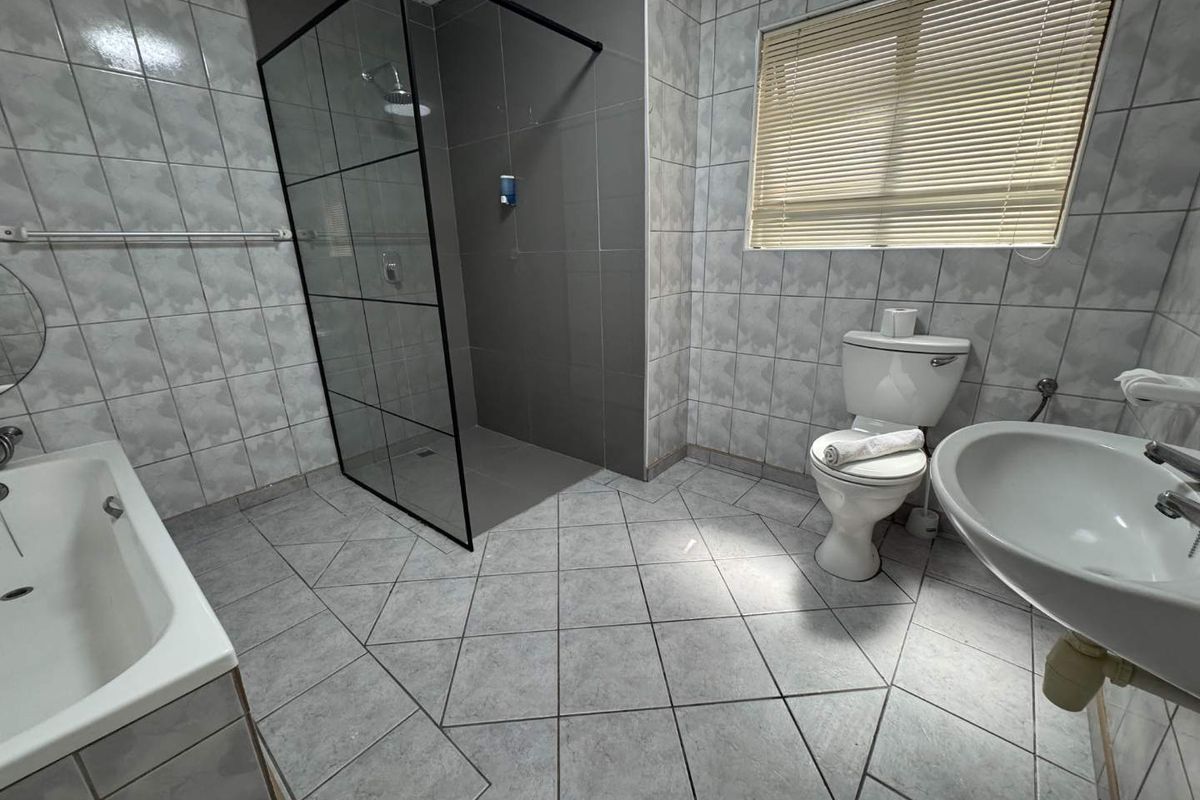 A modern bathroom featuring a walk-in shower with a black frame, a separate bathtub, a pedestal basin, and tiled flooring.