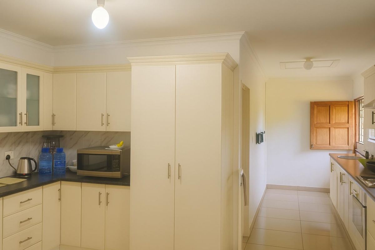 A functional kitchen featuring cream cabinetry, dark countertops, built-in oven, and tiled flooring, leading into a secondary prep or scullery area.