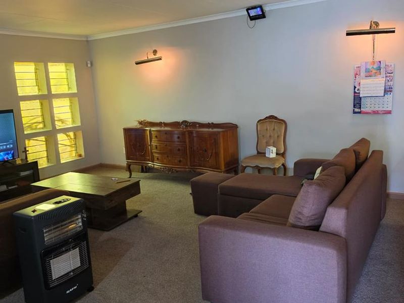 A spacious living room featuring carpeted flooring, louvered windows, and wall-mounted lighting, offering a functional and comfortable living space.