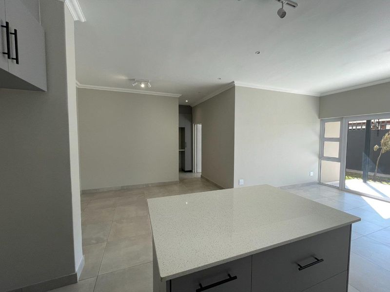 Spacious open-plan living area featuring a modern kitchen island with quartz countertops, neutral tiled flooring, and direct access to an outdoor space.