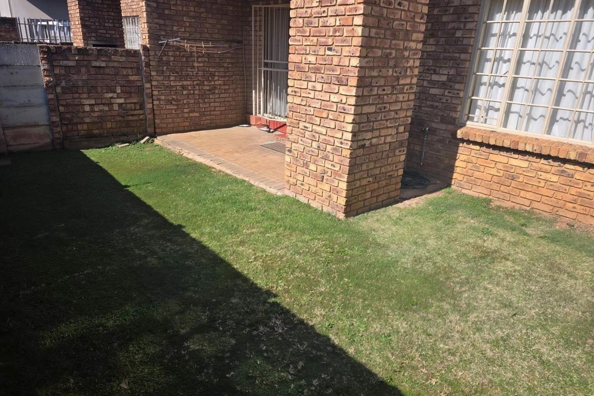 A private rear garden area featuring a paved patio, face brick exterior walls, and a small lawn space.