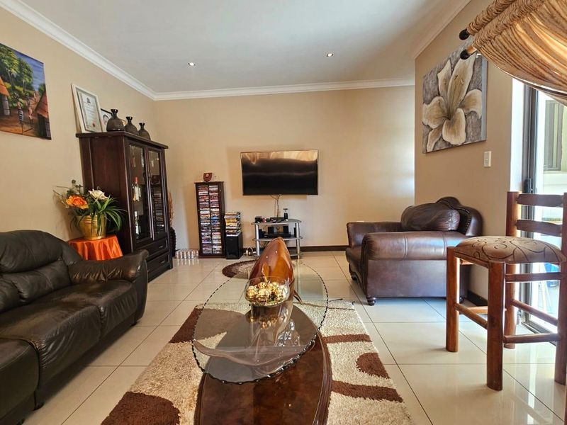 A well-maintained living room featuring neutral tiled flooring, recessed downlighting, and a sliding glass door providing access to the outdoor area.