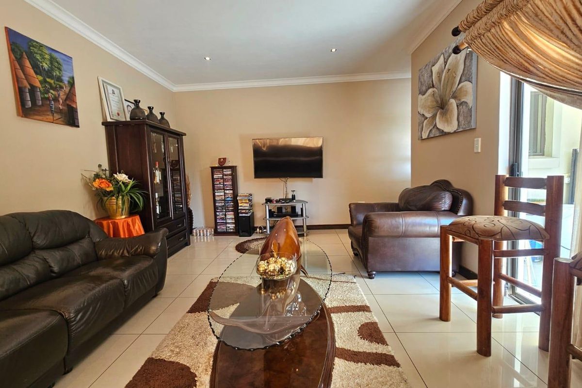A well-maintained living room featuring neutral tiled flooring, recessed downlighting, and a sliding glass door providing access to the outdoor area.