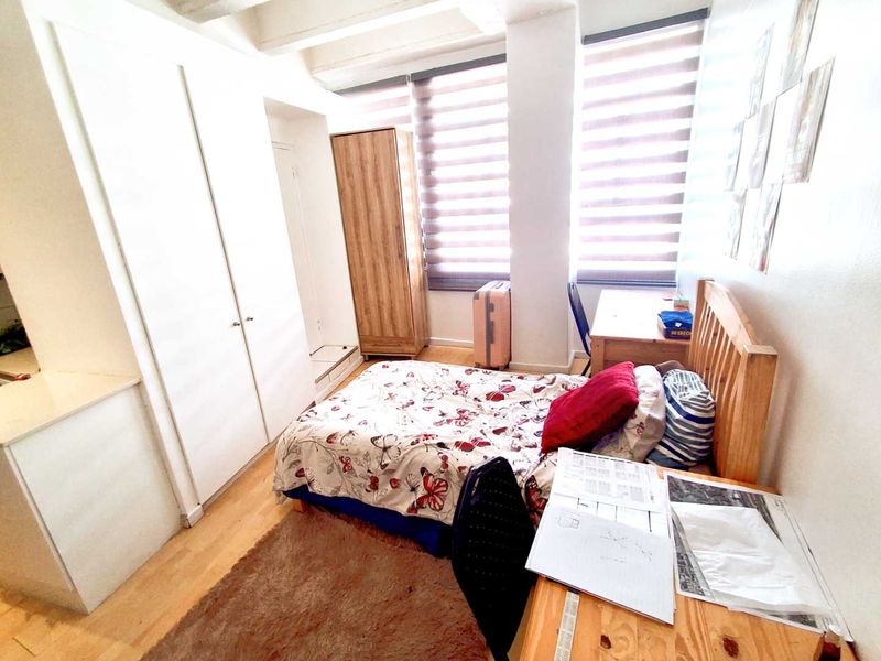 A functional bedroom featuring built-in wardrobes, laminate flooring, and large windows with roller blinds, offering a bright and practical living space.