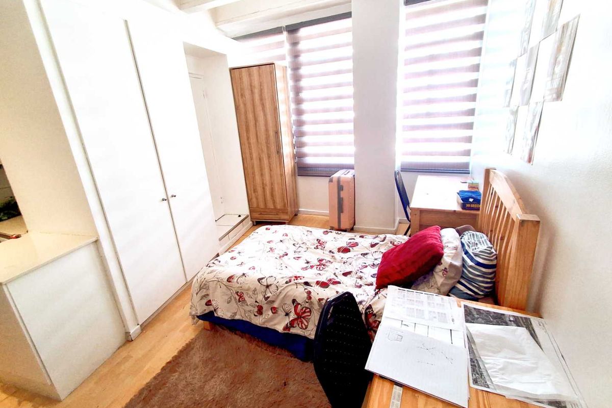A functional bedroom featuring built-in wardrobes, laminate flooring, and large windows with roller blinds, offering a bright and practical living space.
