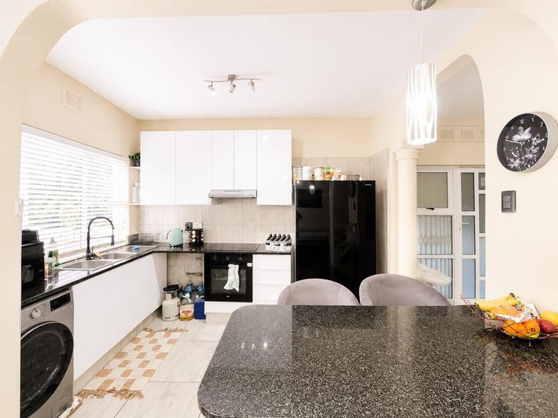 Modern kitchen featuring white cabinetry, granite countertops, integrated oven, extractor fan, and a functional breakfast bar area with tiled flooring.