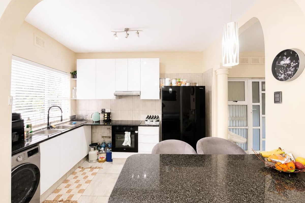 Modern kitchen featuring white cabinetry, granite countertops, integrated oven, extractor fan, and a functional breakfast bar area with tiled flooring.
