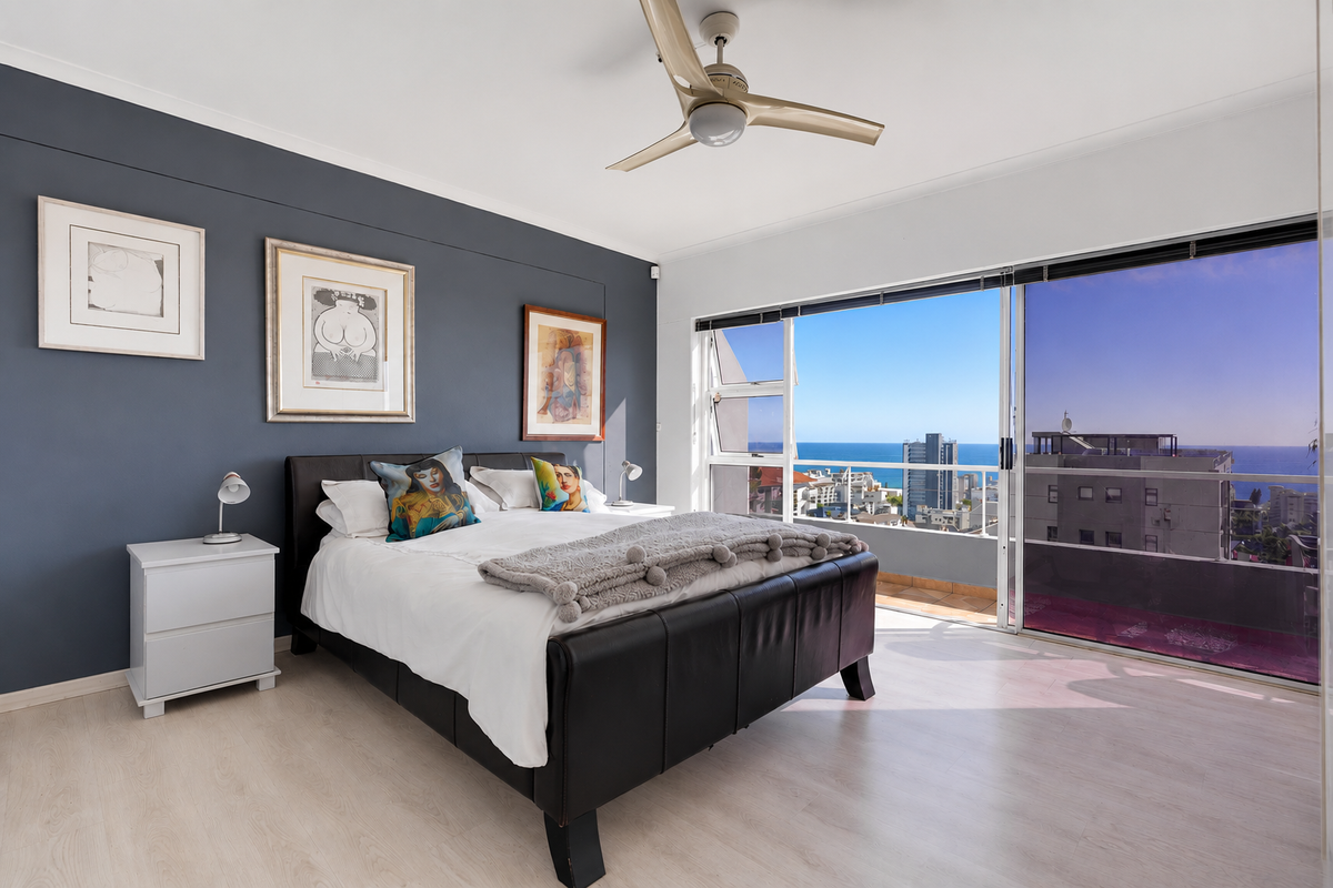 Spacious bedroom featuring laminate flooring, a ceiling fan, and large sliding glass doors opening onto a balcony with coastal city views.