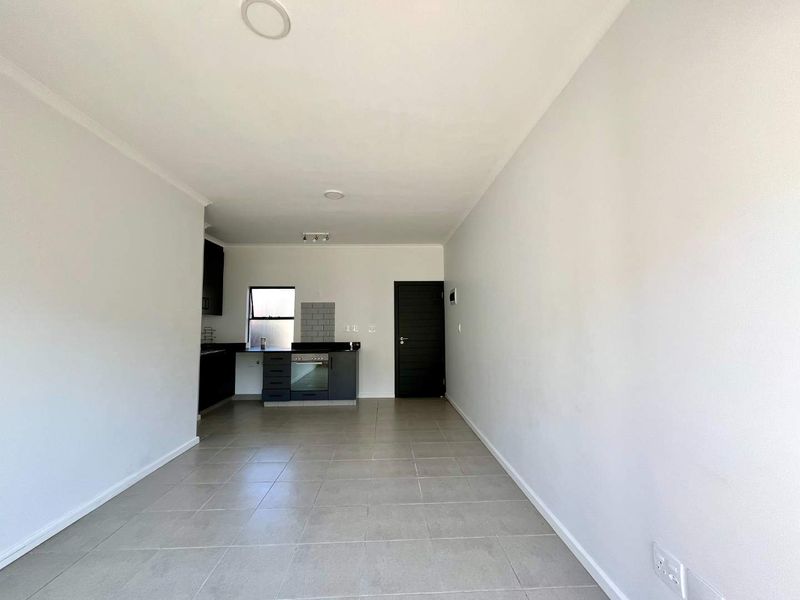 An open-plan living and kitchen area featuring modern dark cabinetry, built-in oven, tiled flooring, and neutral walls, offering a clean and versatile living space.