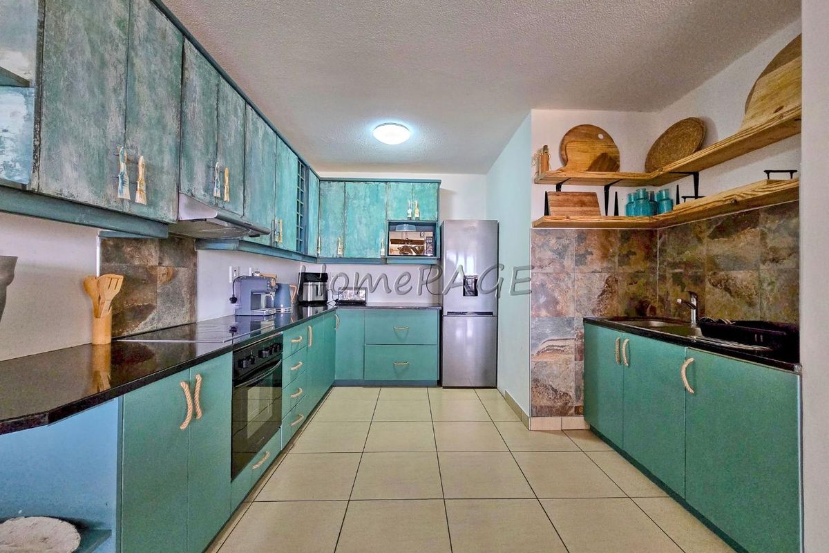 A functional kitchen featuring teal cabinetry, stone tile backsplash, dark stone countertops, and ceramic tile flooring with integrated oven and extractor fan.