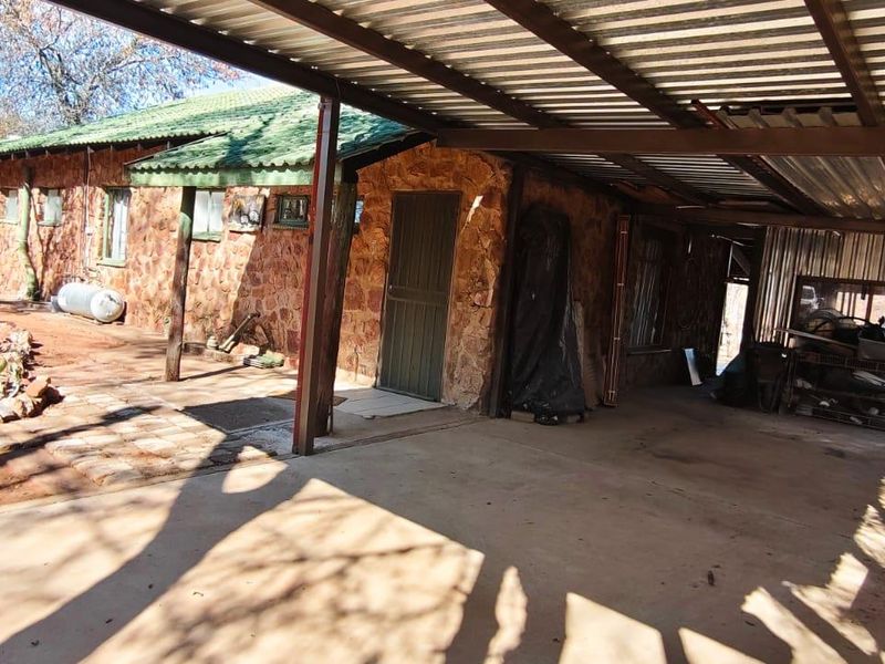 Rear exterior view of a stone-clad house featuring a large metal carport and paved driveway area.