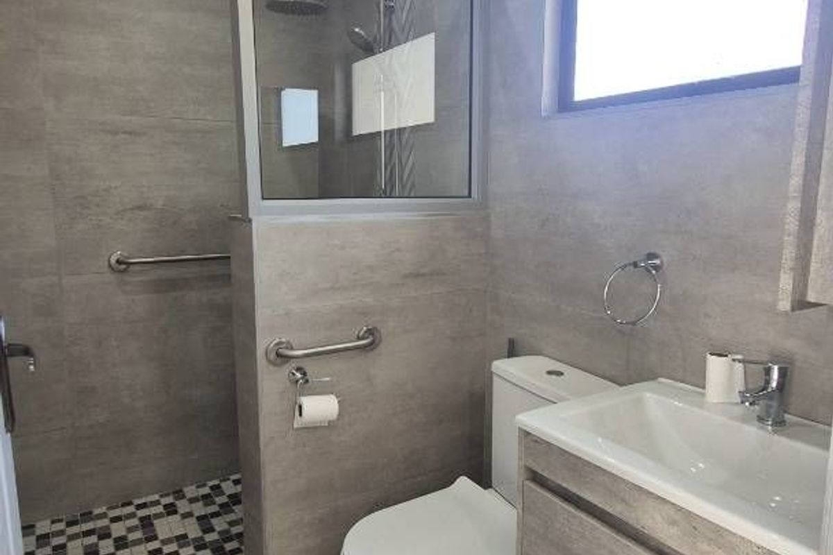 Modern bathroom featuring a walk-in shower with glass partition, wall-mounted vanity with basin, and contemporary grey tiling throughout.