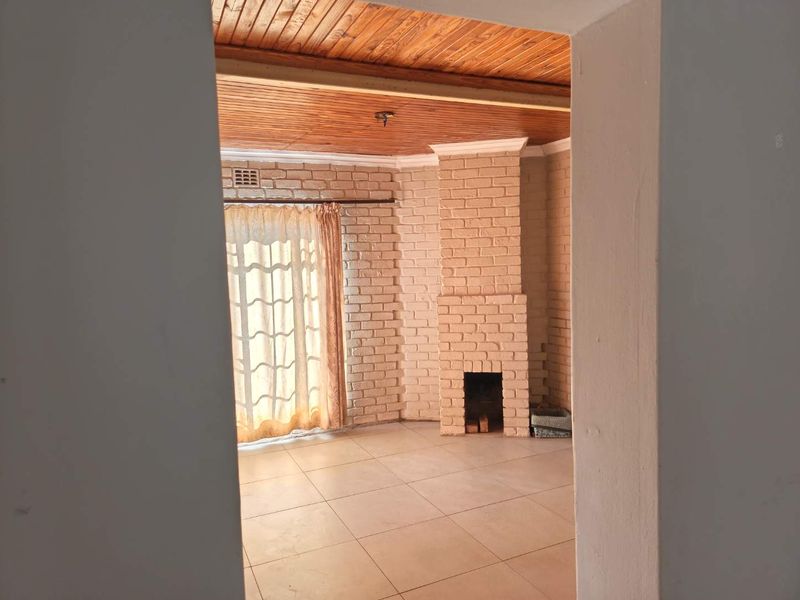 Spacious living room featuring a brick fireplace, timber ceiling, and tiled flooring, offering a blank canvas for potential renovation.