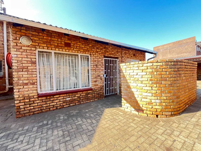 Front exterior view of a face brick townhouse featuring a paved entrance area, security gate, and a private brick wall.