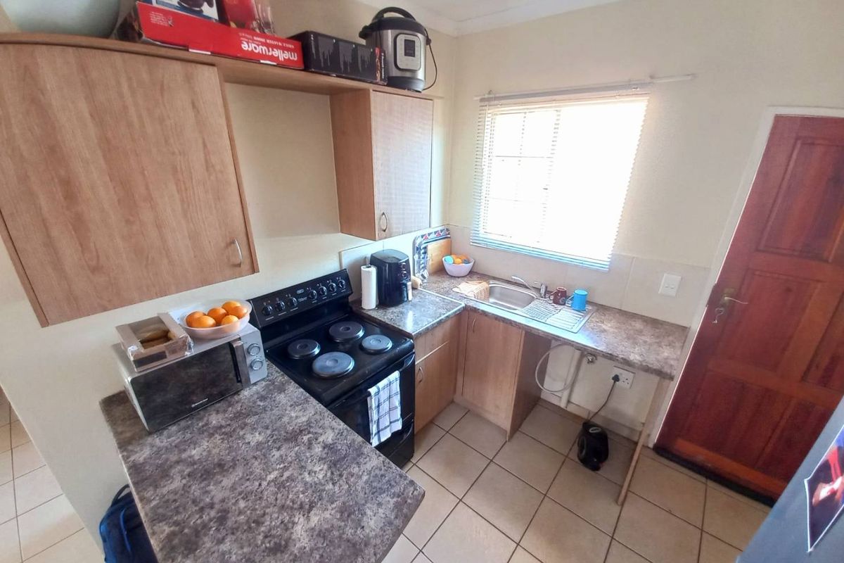 Compact kitchen featuring laminate countertops, built-in cabinetry, a freestanding stove, and tiled flooring with direct access to an exterior door.