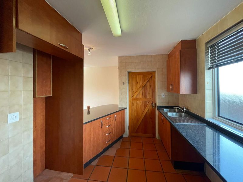A functional kitchen featuring laminate cabinetry, granite countertops, a stainless steel double sink, and tiled flooring, offering a practical layout for renovation.
