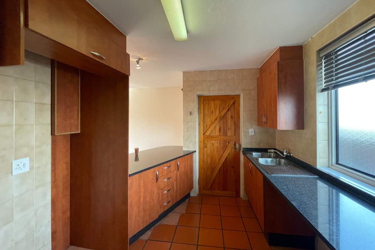A functional kitchen featuring laminate cabinetry, granite countertops, a stainless steel double sink, and tiled flooring, offering a practical layout for renovation.