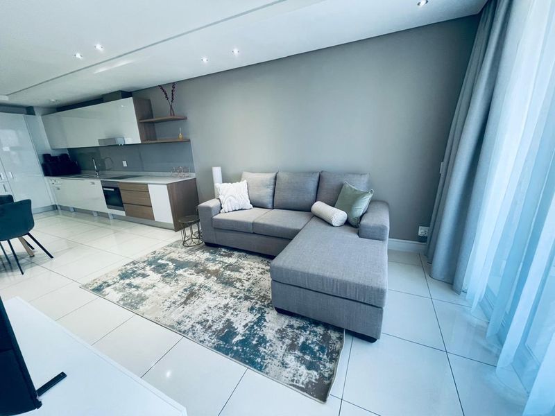 Modern open-plan living area featuring a sleek kitchen with integrated appliances, high-gloss cabinetry, and polished tiled flooring throughout the space.
