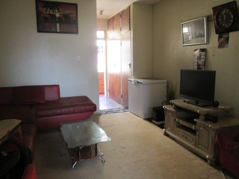 A living room area featuring built-in storage cupboards and access to an adjacent hallway, requiring cosmetic updates to flooring and wall finishes.
