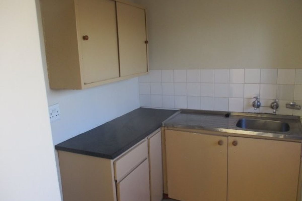 A compact, dated kitchen area featuring original laminate cabinetry, a stainless steel sink, and a tiled backsplash, offering potential for a modern renovation.