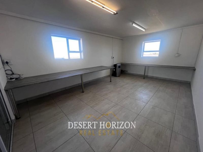 A functional, empty office space featuring tiled flooring, built-in desk surfaces, and overhead fluorescent lighting, suitable for a workspace or studio.