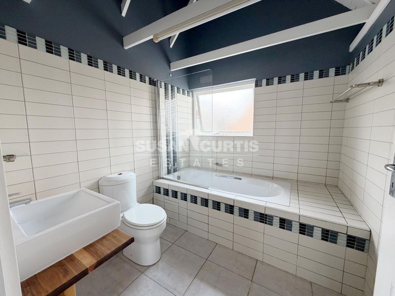 A functional bathroom featuring a built-in bathtub with a glass screen, tiled finishes, and exposed ceiling beams.