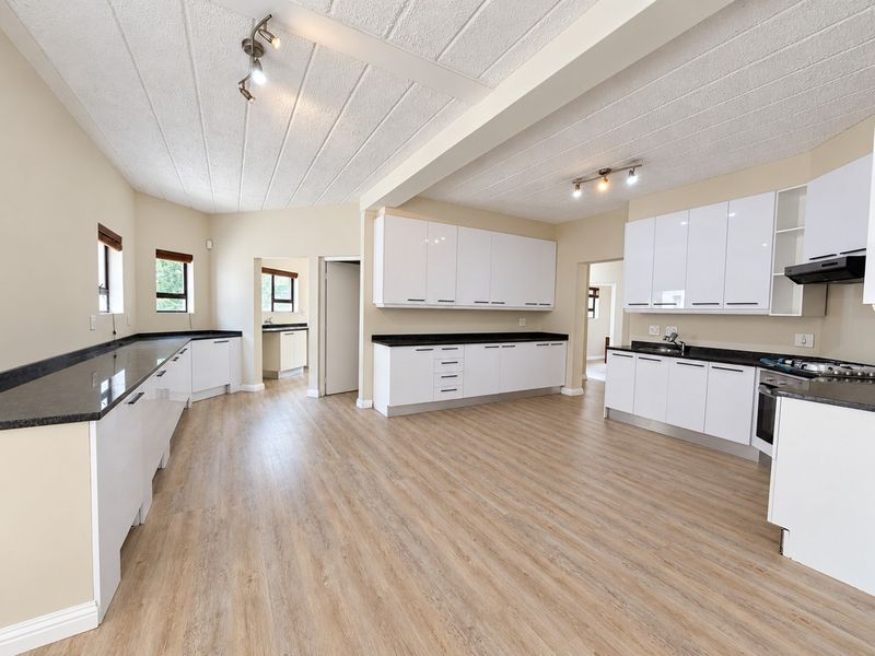 Spacious, modern kitchen featuring white cabinetry, dark granite countertops, built-in appliances, and light wood-look laminate flooring in an open-plan layout.
