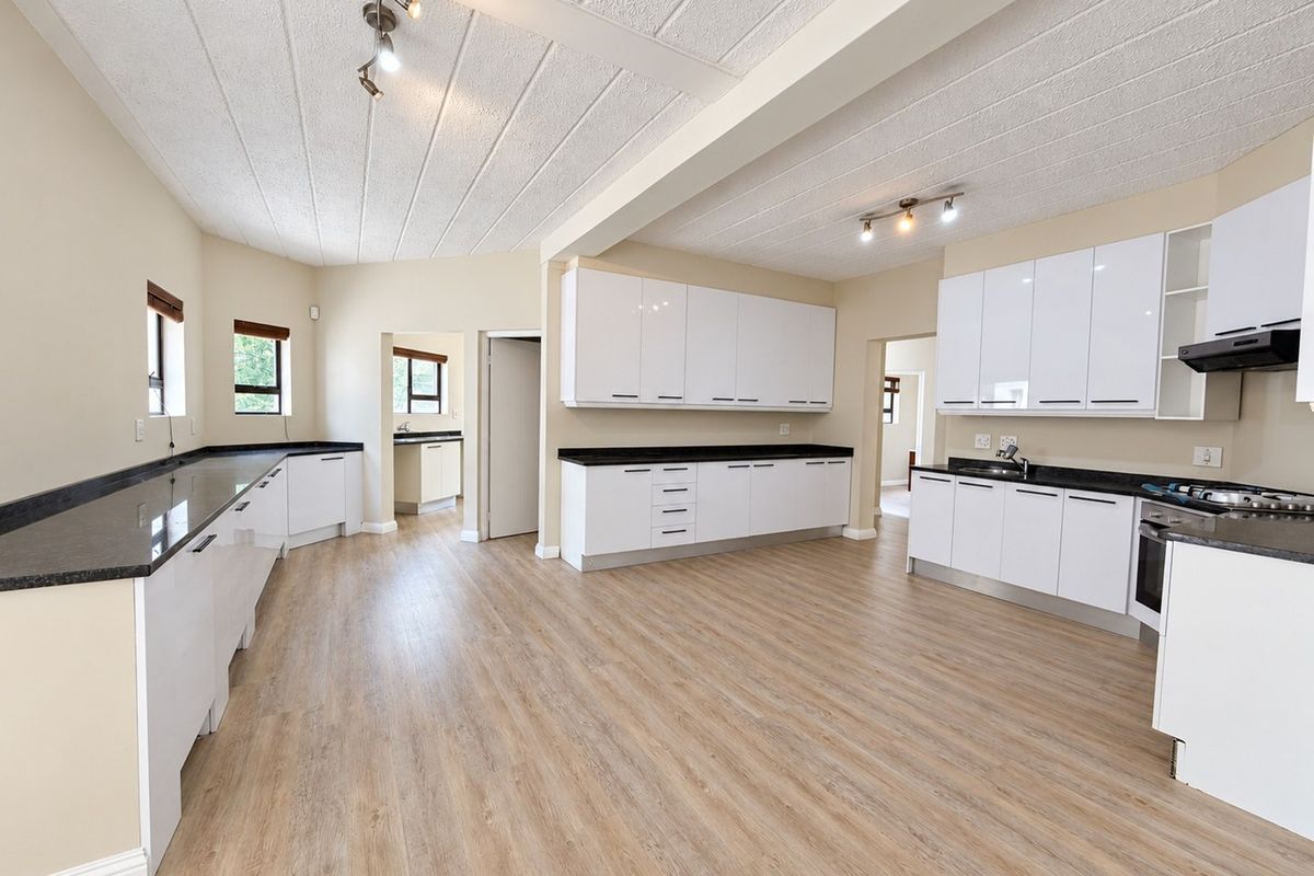 Spacious, modern kitchen featuring white cabinetry, dark granite countertops, built-in appliances, and light wood-look laminate flooring in an open-plan layout.