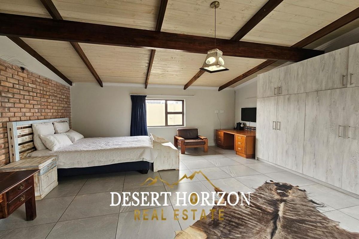 Spacious bedroom featuring exposed timber ceiling beams, a rustic brick feature wall, and extensive built-in cabinetry with light wood-grain finish.