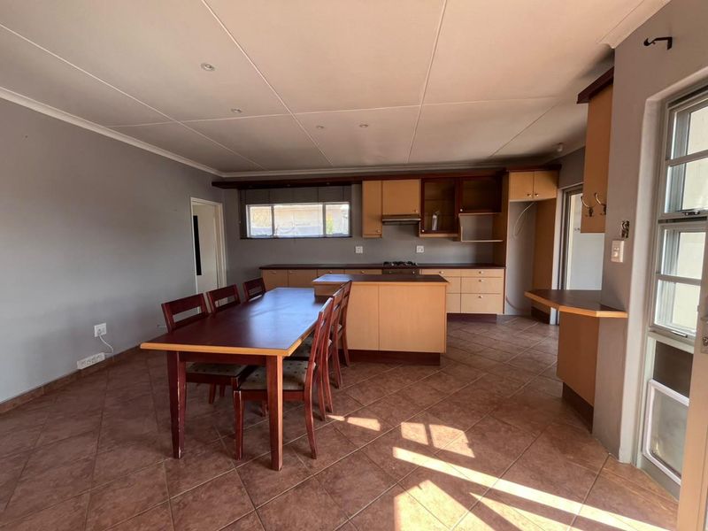 Open-plan kitchen and dining area featuring wooden cabinetry, a central island, hob, extractor fan, and tiled flooring throughout.