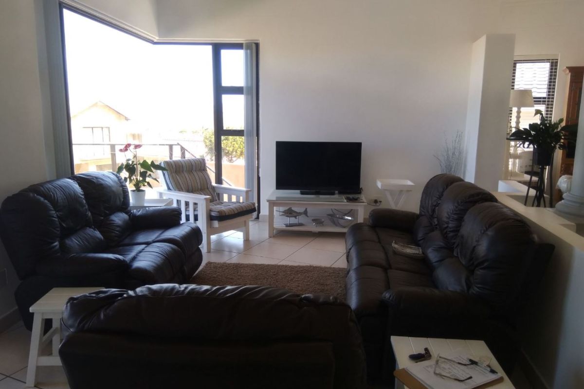 A bright living room featuring large windows with access to an outdoor balcony, tiled flooring, and an open-plan layout.