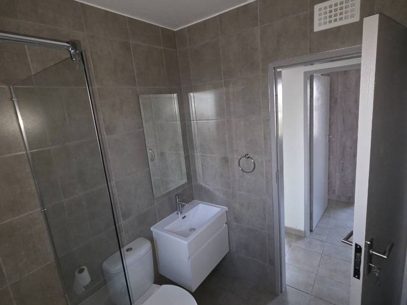 A modern, clean bathroom featuring a wall-mounted vanity, toilet, and a bathtub with a glass shower screen, finished with neutral wall and floor tiles.