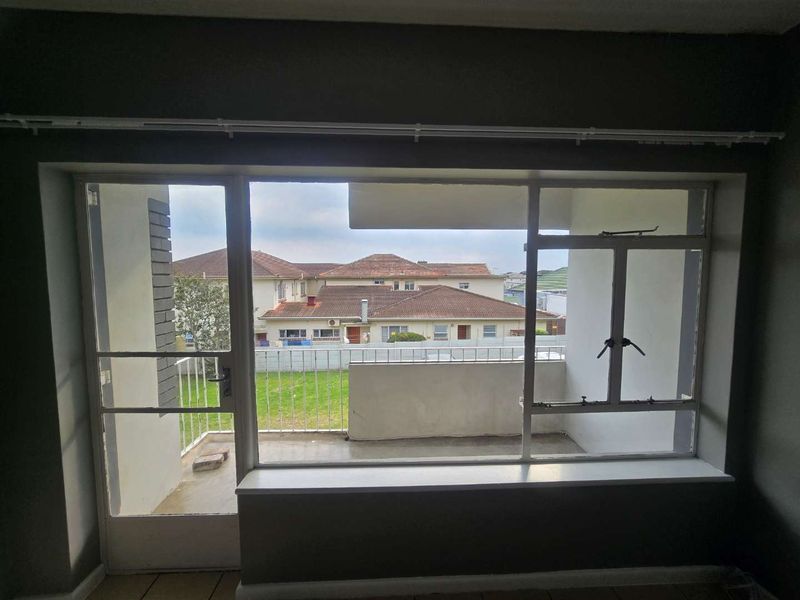 An empty living room featuring large windows and a door providing direct access to an outdoor balcony area.