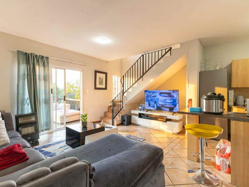 Open-plan living area featuring tiled floors, a staircase with metal railing, and a kitchen with built-in cabinetry and a breakfast bar.