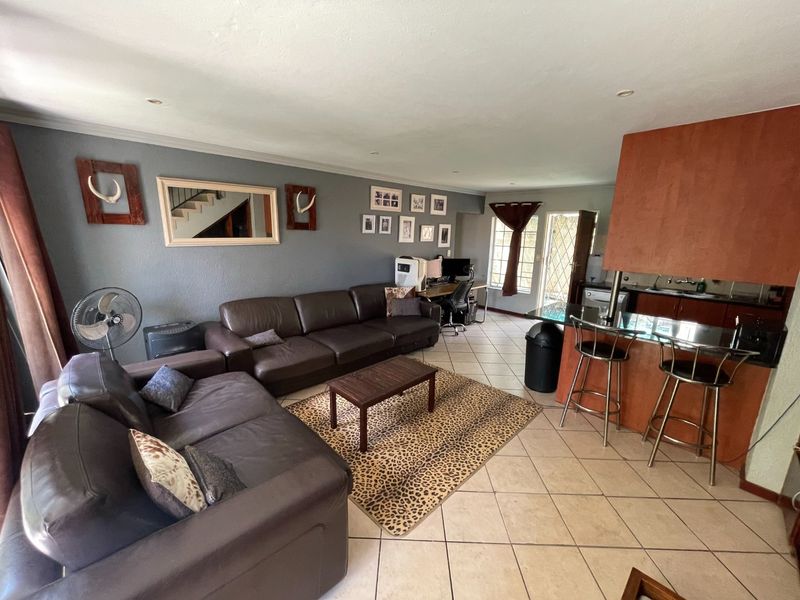 Open-plan living area featuring tiled flooring, a breakfast bar with integrated kitchen cabinetry, and direct access to the exterior through a security gate.