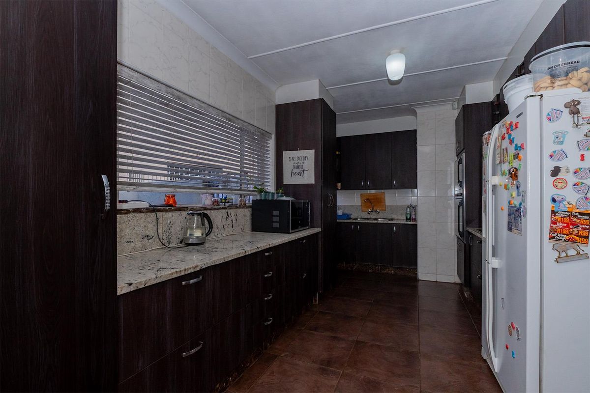 A functional kitchen featuring dark wood cabinetry, granite countertops, tiled splashbacks, and tiled flooring with a galley-style layout.
