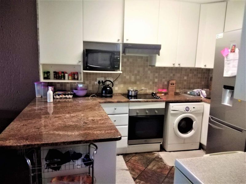 Functional kitchen featuring granite countertops, built-in oven, electric hob, extractor fan, and ample cabinetry with integrated space for a washing machine.