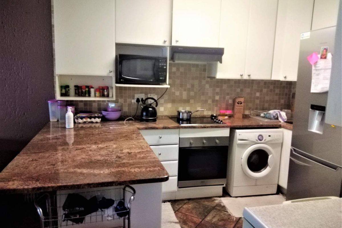 Functional kitchen featuring granite countertops, built-in oven, electric hob, extractor fan, and ample cabinetry with integrated space for a washing machine.