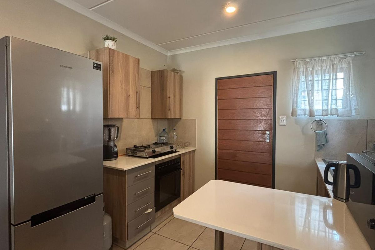 A functional kitchen featuring modern wood-finish cabinetry, stone countertops, a gas hob, built-in oven, and tiled flooring.