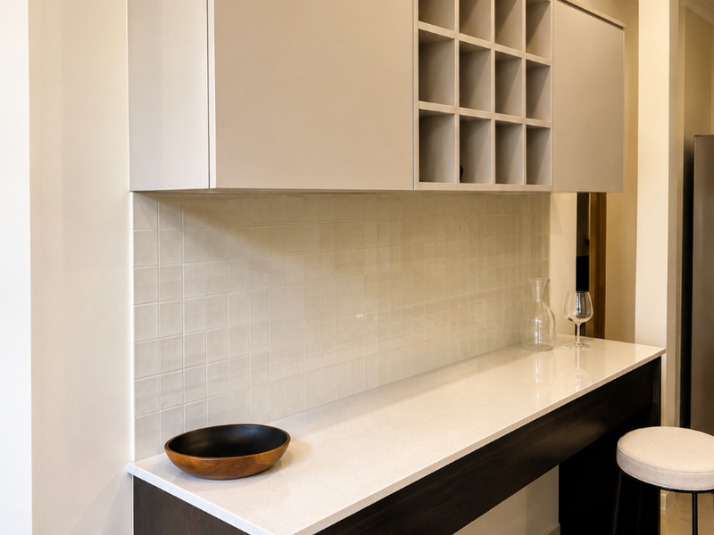 A modern kitchen breakfast bar area featuring sleek built-in cabinetry, a wine rack, stone countertops, and a neutral tiled backsplash.